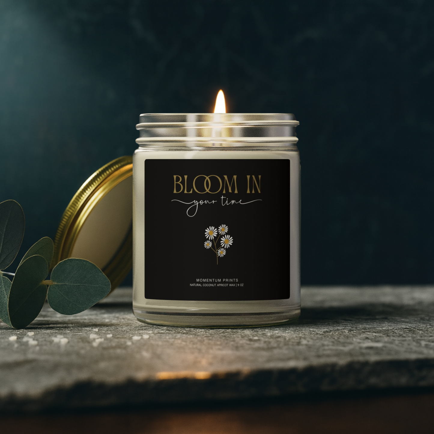 Bloom in Your Time” black-label candle styled with eucalyptus on dark moody background — premium aesthetic by Momentum Prints.