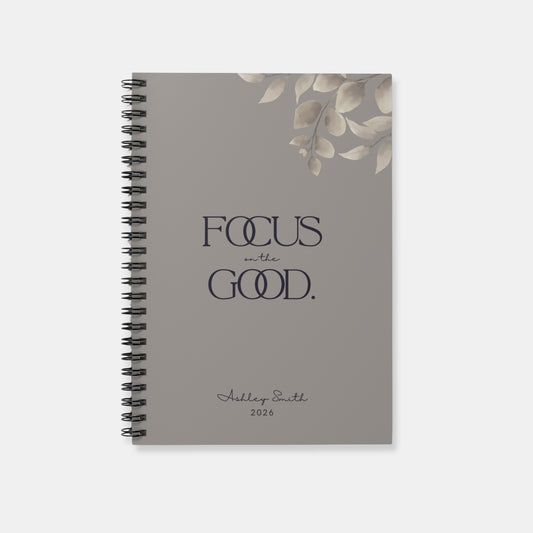 Personalized “Focus on the Good” spiral notebook in warm gray with minimalist botanical detail and refined typography.