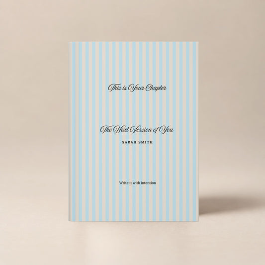 Premium personalized hardcover journal with a sky blue striped cover and black script lettering, shown standing upright on a soft beige background by Momentum Prints.