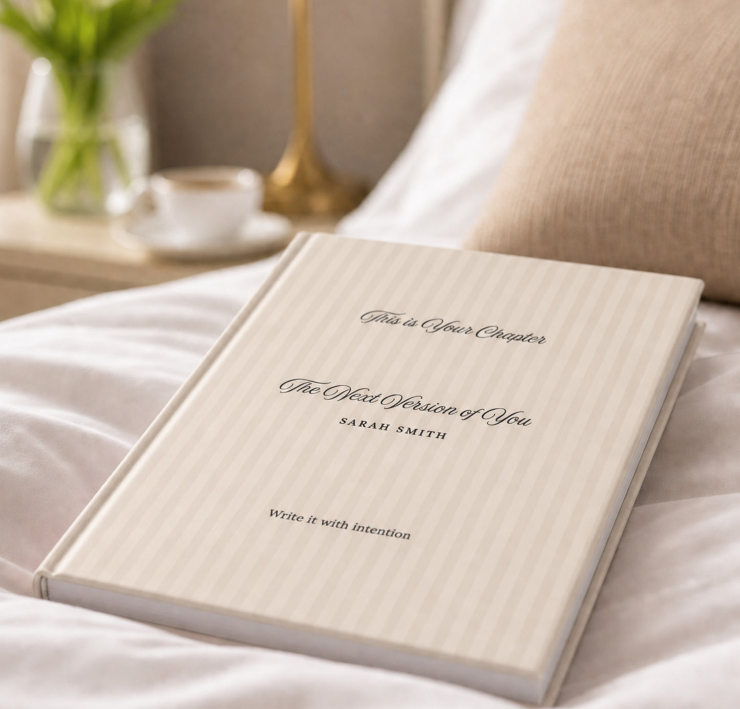 Premium personalized hardcover journal with soft beige striped cover resting on a bed, styled beside a cup of coffee, fresh greenery, and a warm knit pillow in a cozy lifestyle setting by Momentum Prints.