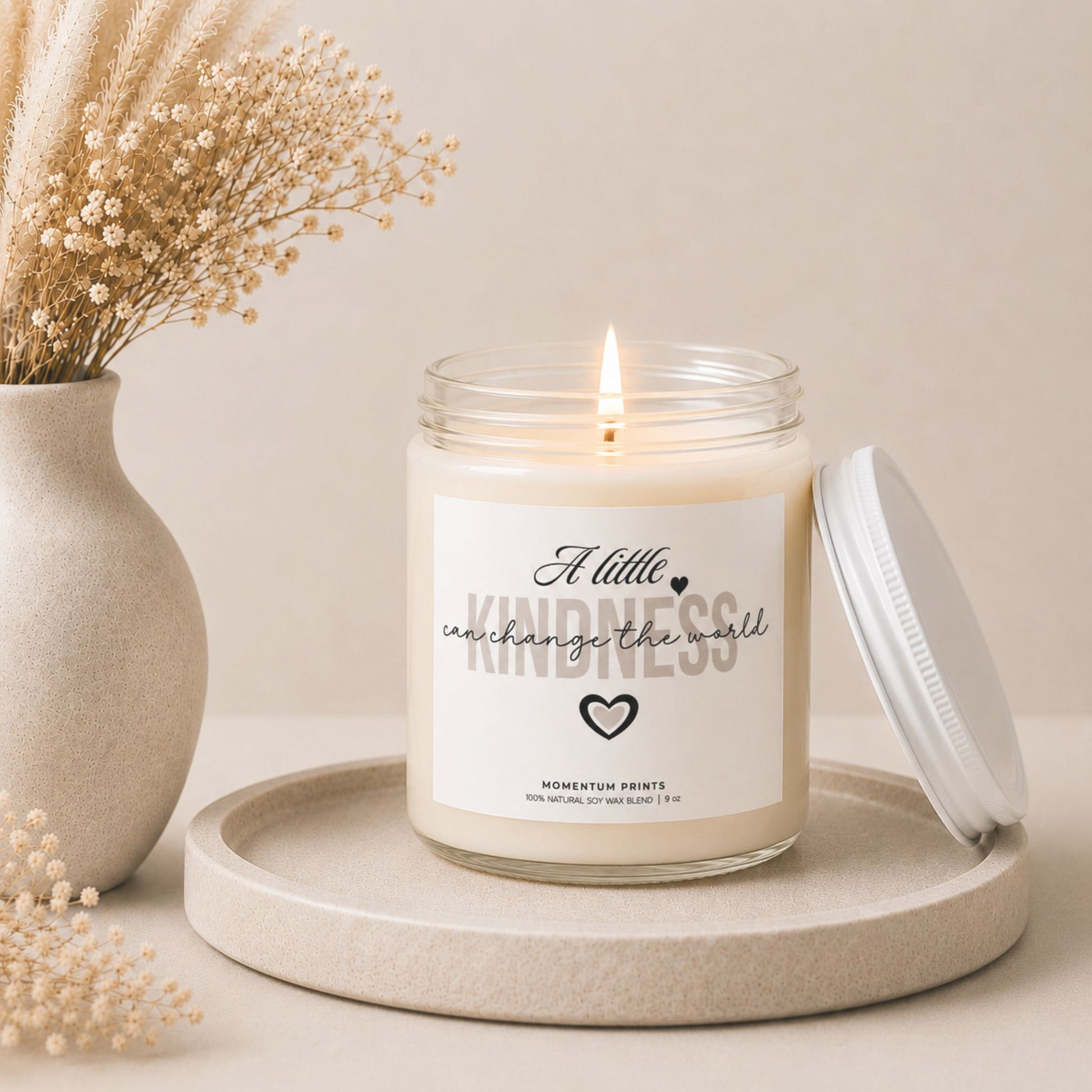A Little Kindness Can Change the World soy candle by Momentum Prints burning softly beside dried flowers in a warm minimalist self-care and home decor setting.