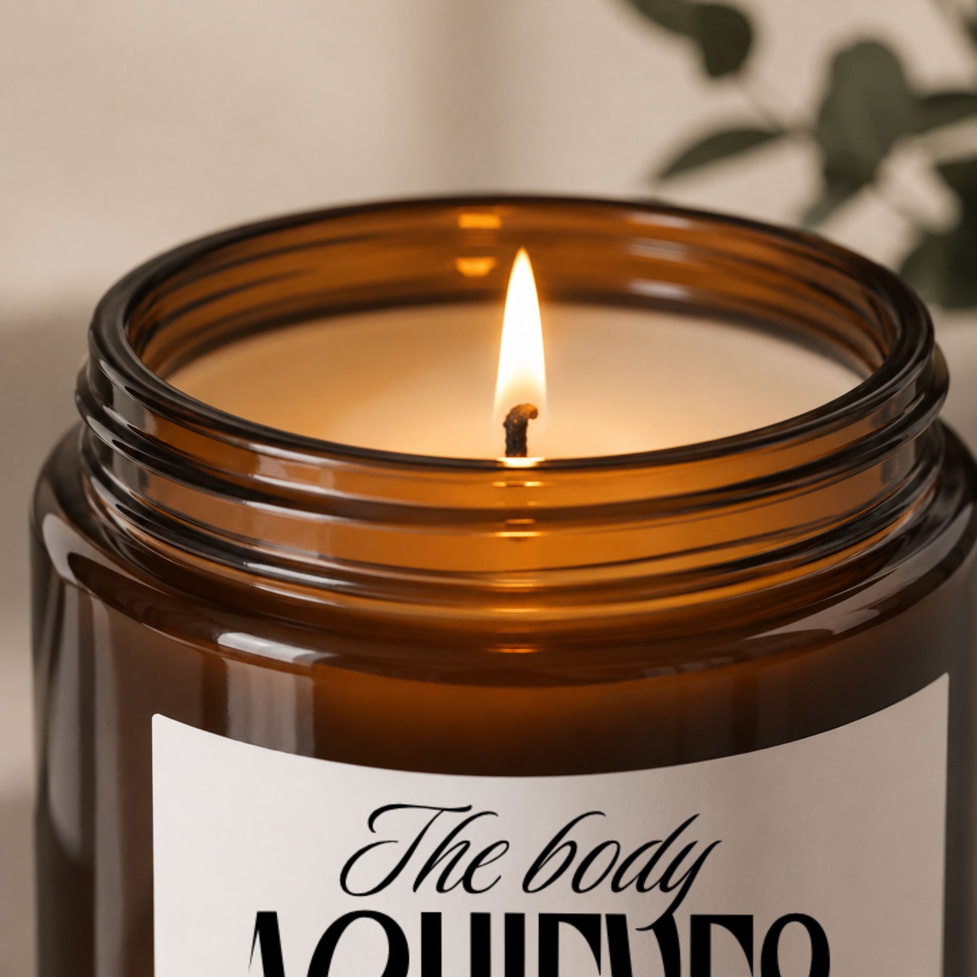 Close-up of a luxury amber glass soy candle with a minimalist motivational label, featuring a sharp glowing flame, smooth cream wax surface, and soft warm lighting in a cozy neutral setting.