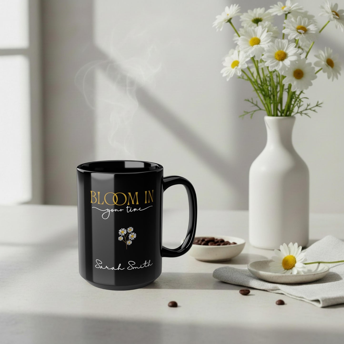 Personalized black ceramic mug with “Bloom in Your Time” design in a soft neutral scene with white daisies and steam rising.