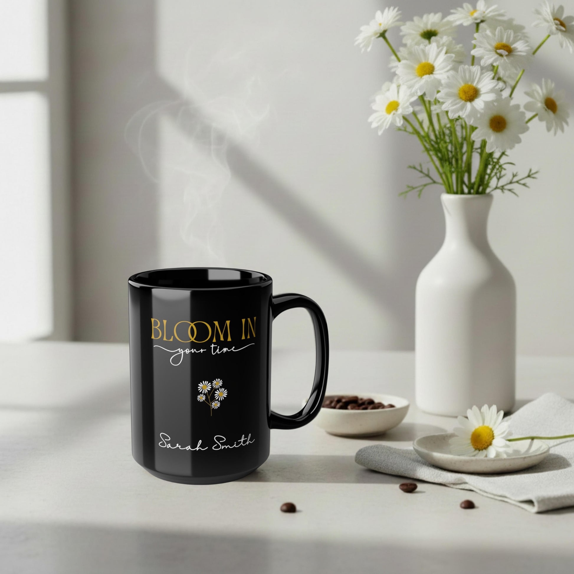 Personalized black ceramic mug with “Bloom in Your Time” design in a soft neutral scene with white daisies and steam rising.