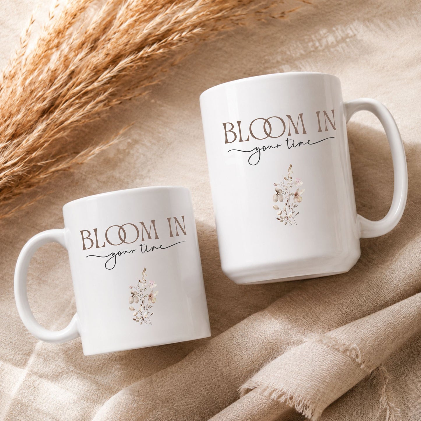 Flat lay arrangement of Bloom in Your Time ceramic mugs on textured neutral fabric with dried botanical elements and warm natural lighting.