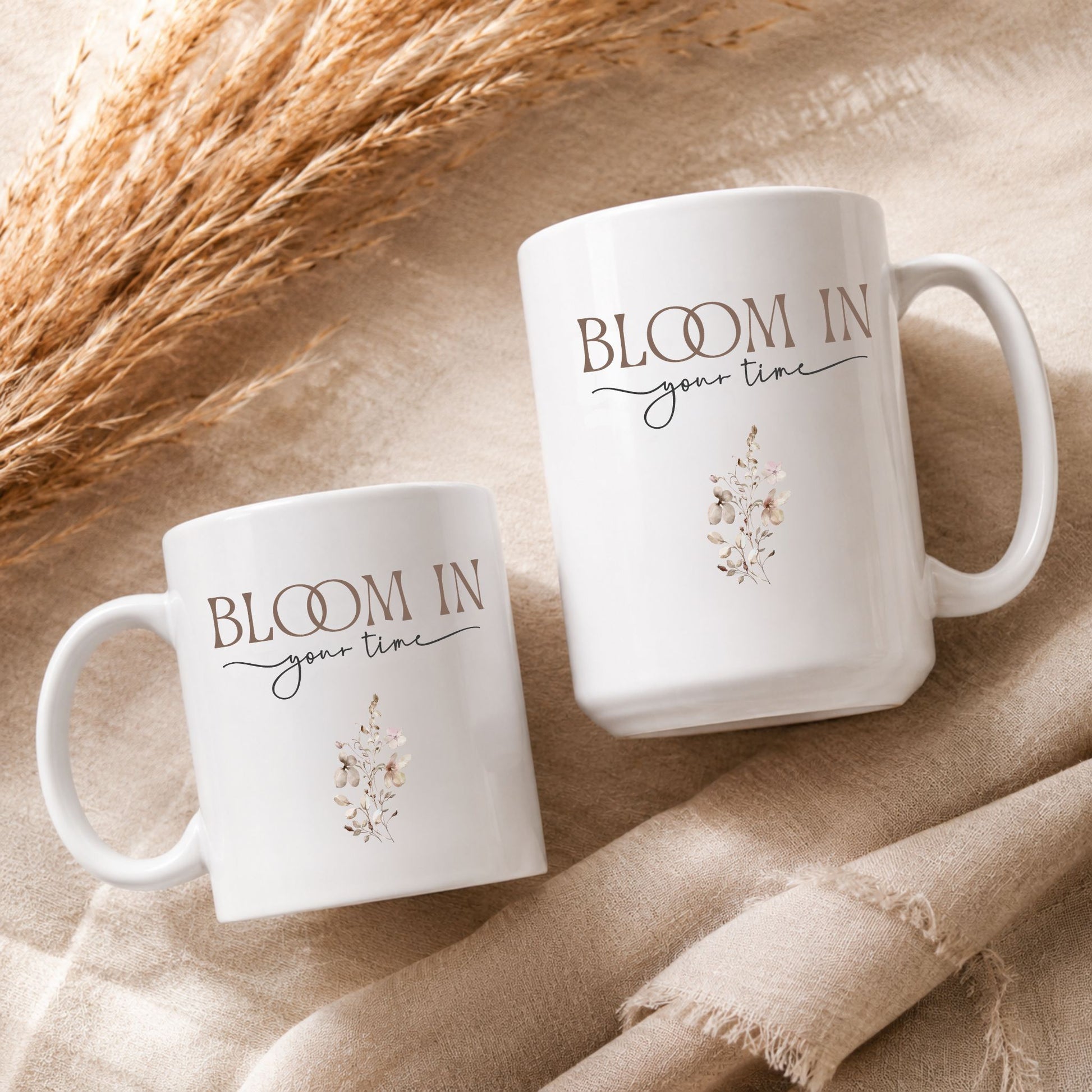 Flat lay arrangement of Bloom in Your Time ceramic mugs on textured neutral fabric with dried botanical elements and warm natural lighting.