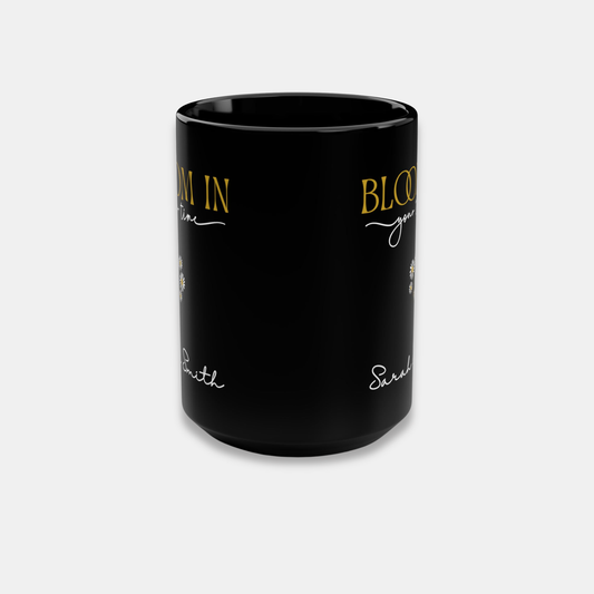 Black personalized mug side wrap view showing partial “Bloom in Your Time” artwork and name detail on a light background.