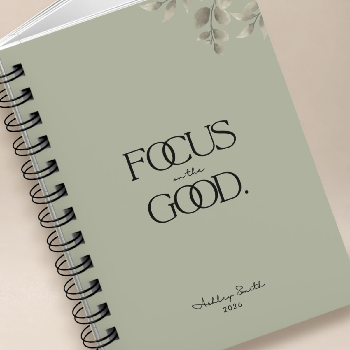 Close-up detail of a personalized dried sage spiral notebook cover, showing the black lettering, muted botanical illustration, and script name personalization. Momentum Prints.