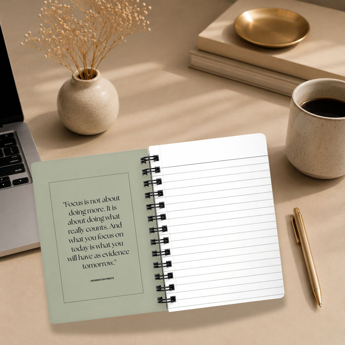 The open interior of a personalized dried sage spiral notebook, showing a printed reflection on focus and intention beside a blank lined page, styled with a laptop, dried baby's breath, and coffee.