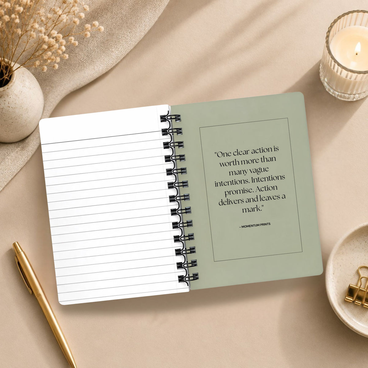 The open interior of a personalized dried sage spiral notebook, showing a blank lined page beside a printed message about taking clear action, styled with a lit candle, dried baby's breath, and gold binder clips.