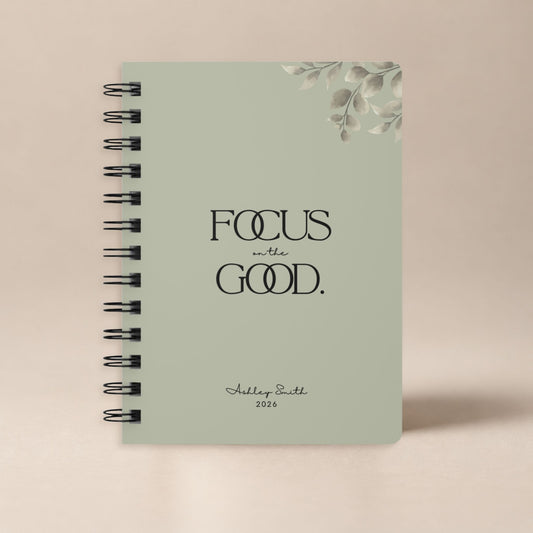 A personalized dried sage spiral notebook standing upright against a plain warm neutral backdrop, shown as a clean product hero shot.