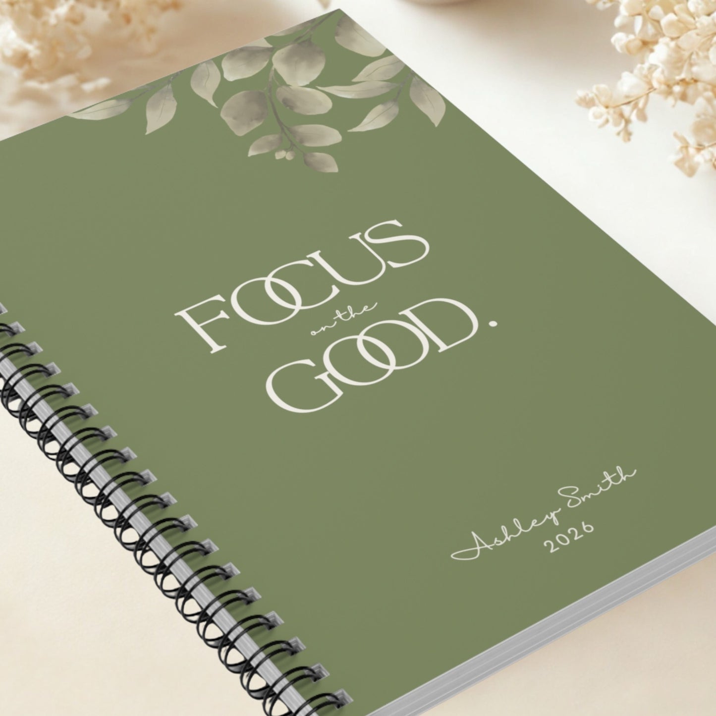 Olive green spiral notebook “Focus on the Good” with elegant leaf detail, premium minimal design close-up.