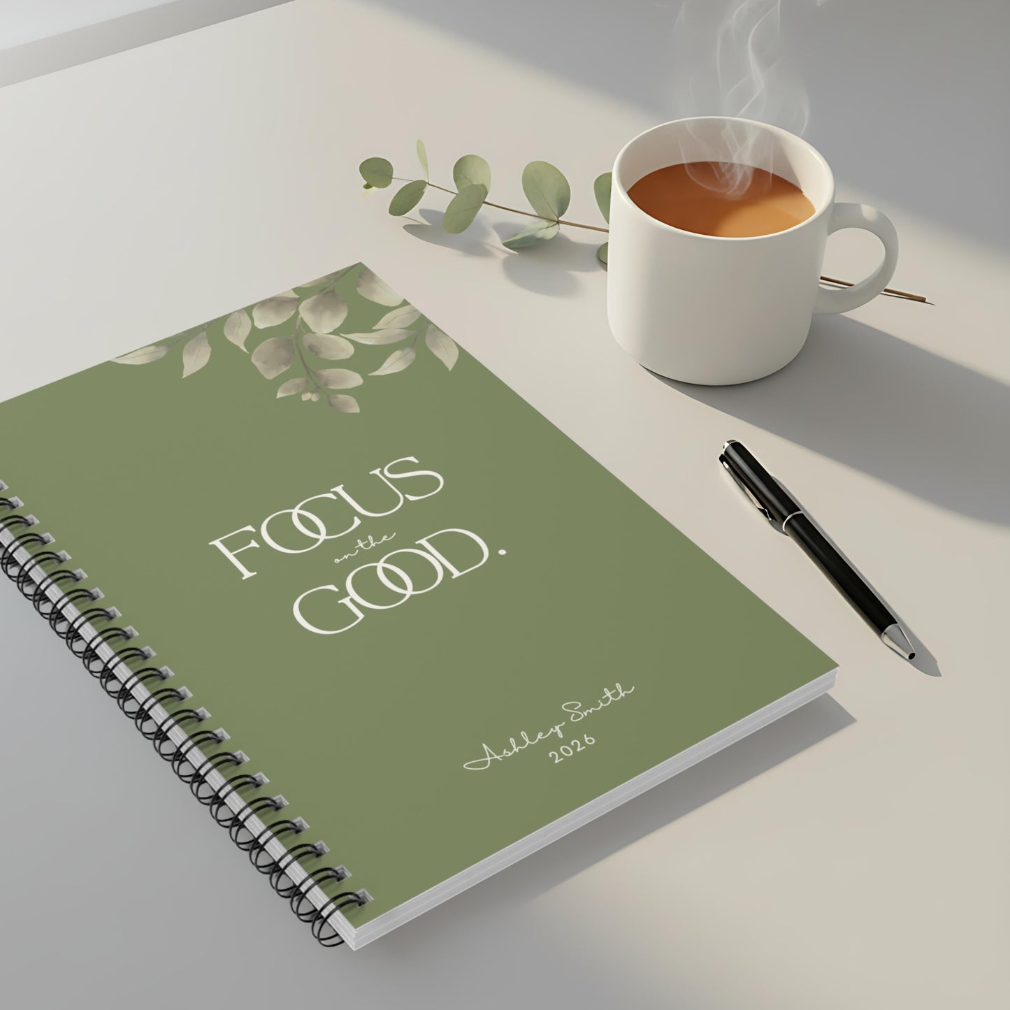 Olive green spiral notebook “Focus on the Good” on modern desk with coffee mug, premium productivity setup.