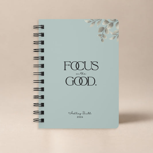 A personalized pale sky spiral notebook standing upright against a plain warm neutral backdrop, shown as a clean product hero shot.