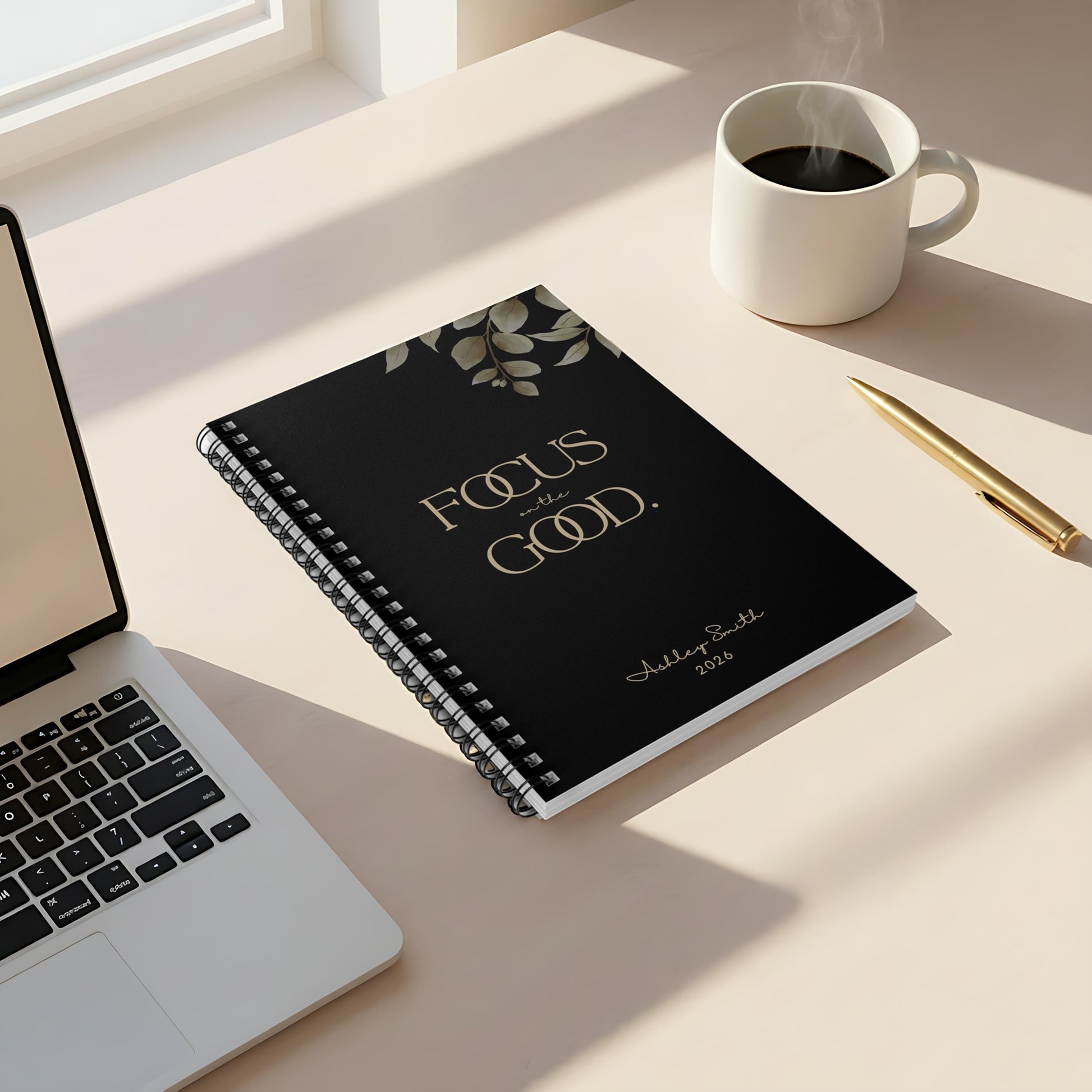 Momentum Prints motivational spiral notebook (6x8) in Midnight Black featuring the “Focus on the Good” cover on a minimalist desk with coffee and soft window light.