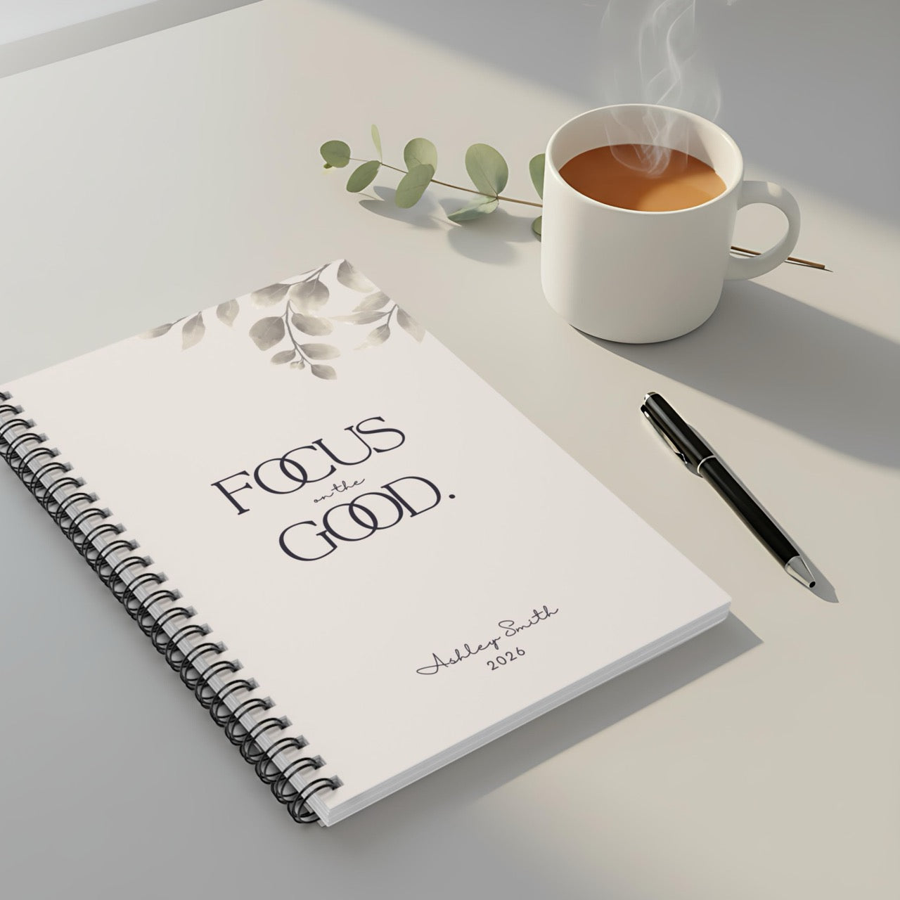 Spiral notebook with “Focus on the Good” cover styled with coffee cup and neutral decor in a cozy workspace