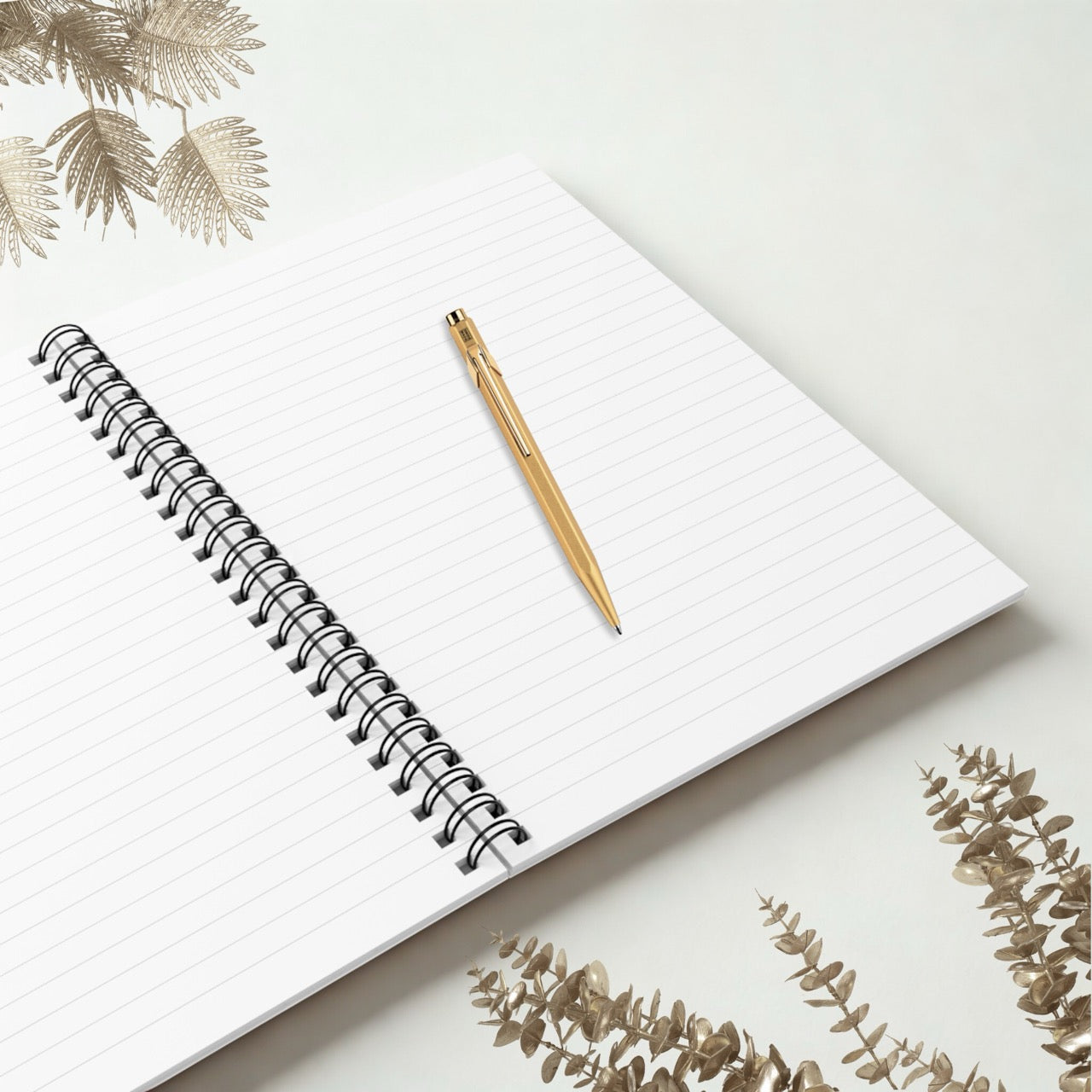 Open spiral notebook showing lined pages with a gold pen on a neutral minimal background