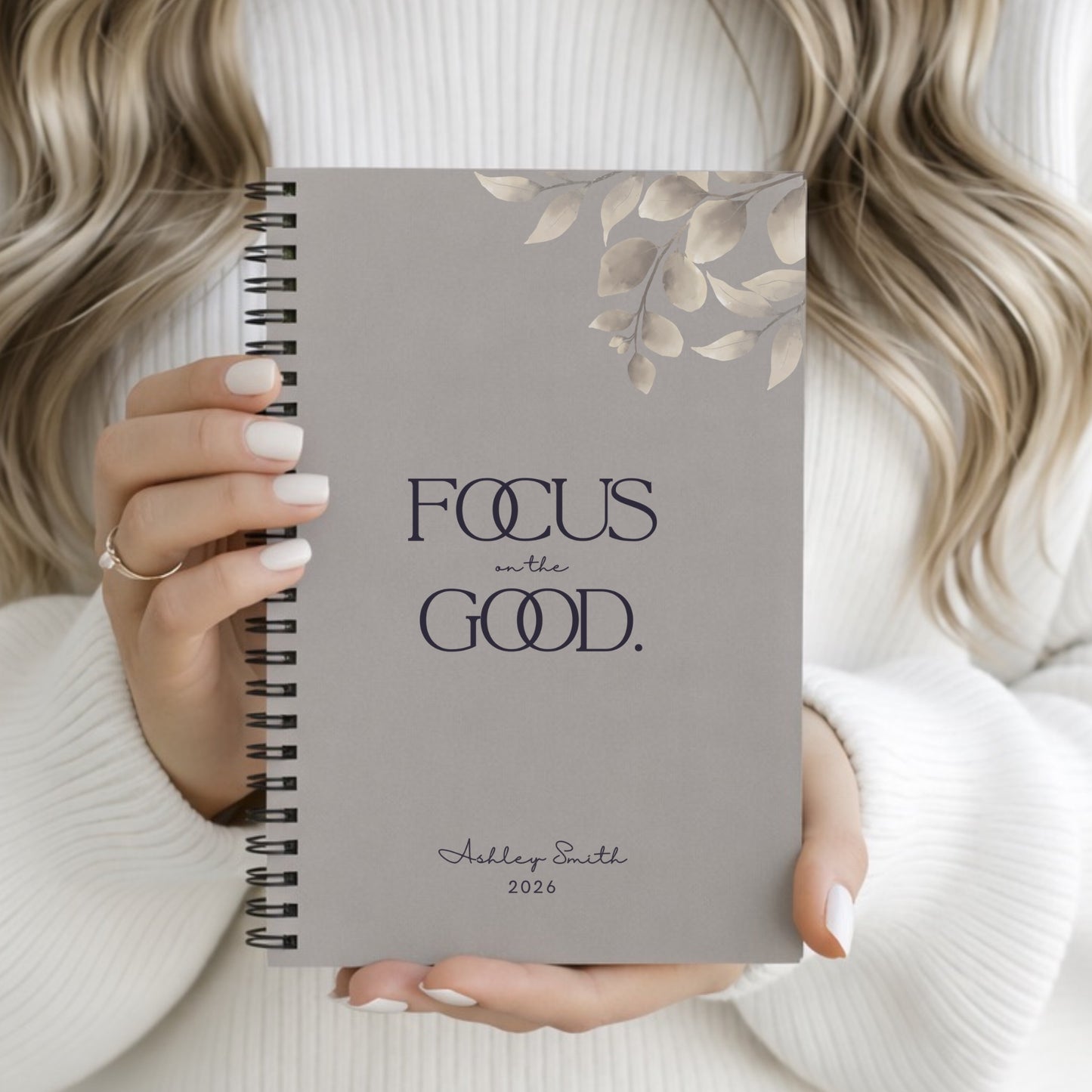 Woman holding Focus on the Good warm gray spiral notebook in a soft neutral aesthetic setting.