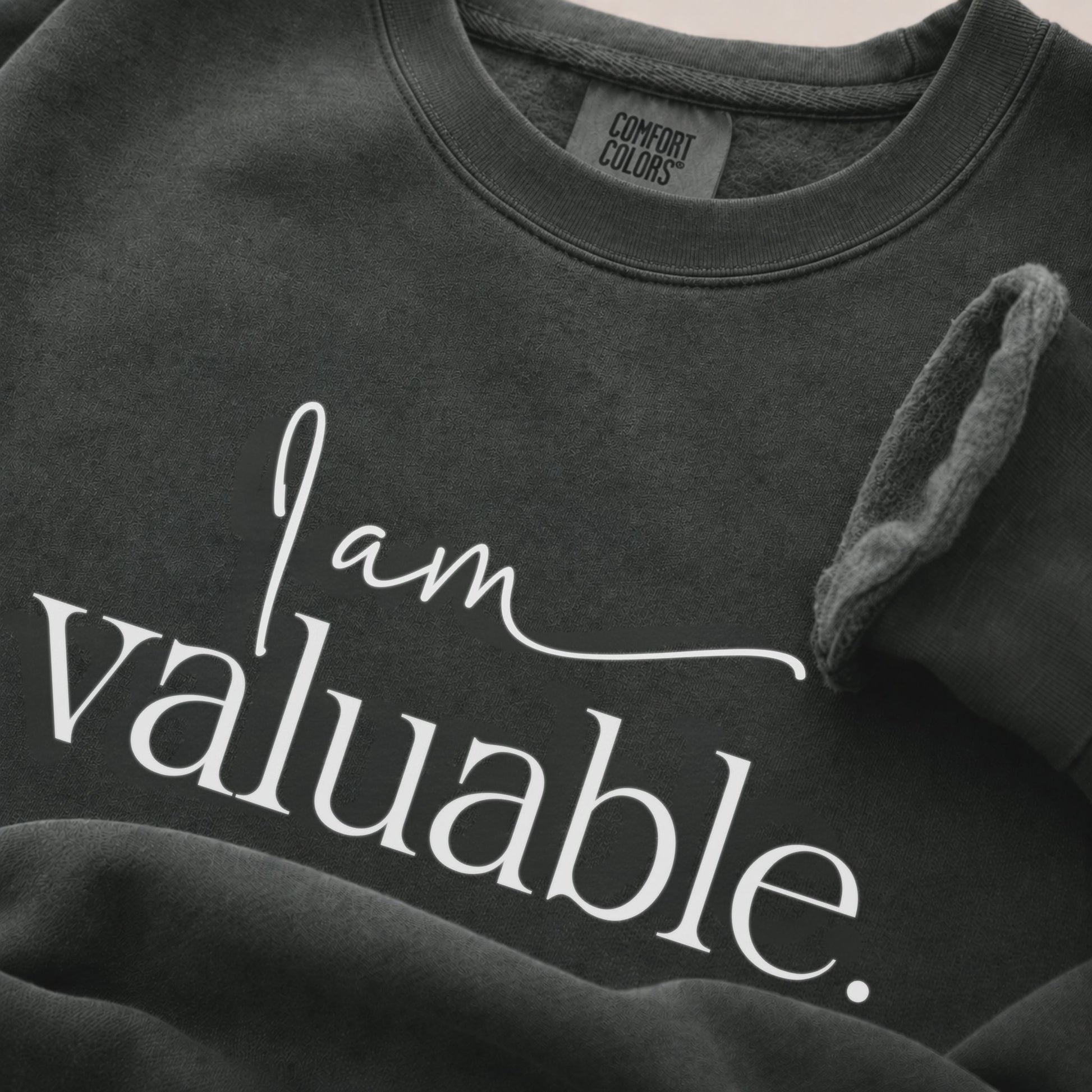 Close-up detail of a pepper Comfort Colors sweatshirt featuring soft garment-dyed fabric, ribbed crew neck, and premium cotton texture in a minimalist neutral setting.