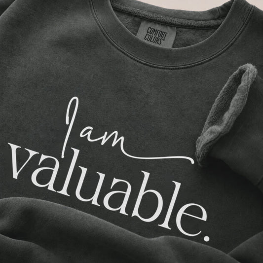 Close-up detail of a pepper Comfort Colors sweatshirt featuring soft garment-dyed fabric, ribbed crew neck, and premium cotton texture in a minimalist neutral setting.