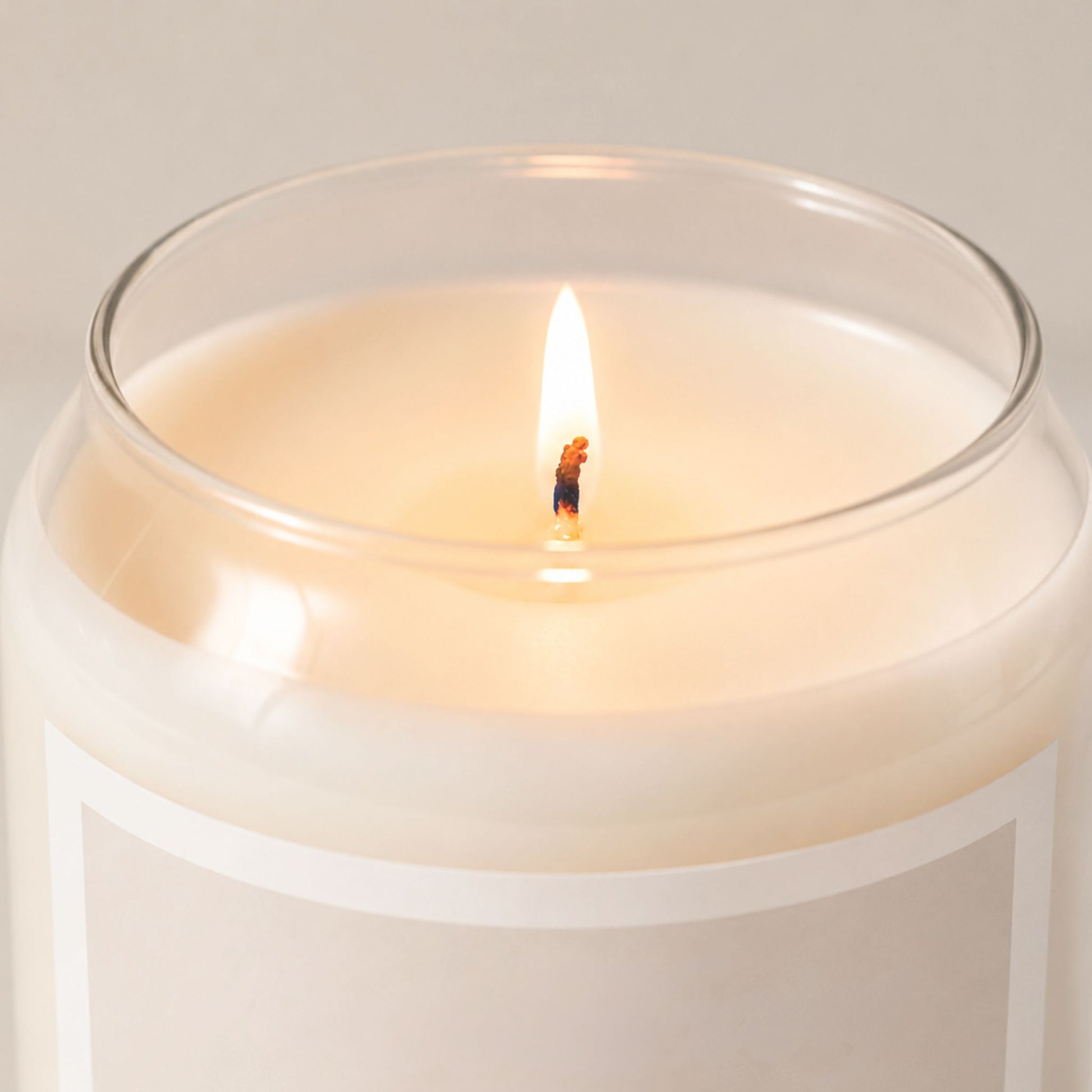 Close-up of a lit minimalist soy candle in a clear glass jar with creamy wax and a soft beige label featuring the phrase “Keep Moving,” styled with warm neutral lighting and a clean editorial background.