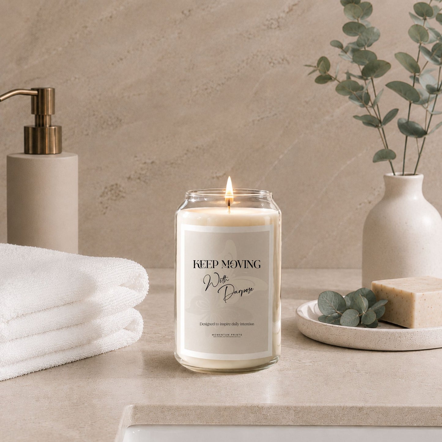 Luxury soy candle with “Keep Moving With Purpose” label styled in a minimalist spa bathroom setting with folded white towels, eucalyptus stems, natural soap, and soft beige stone textures under warm ambient lighting.