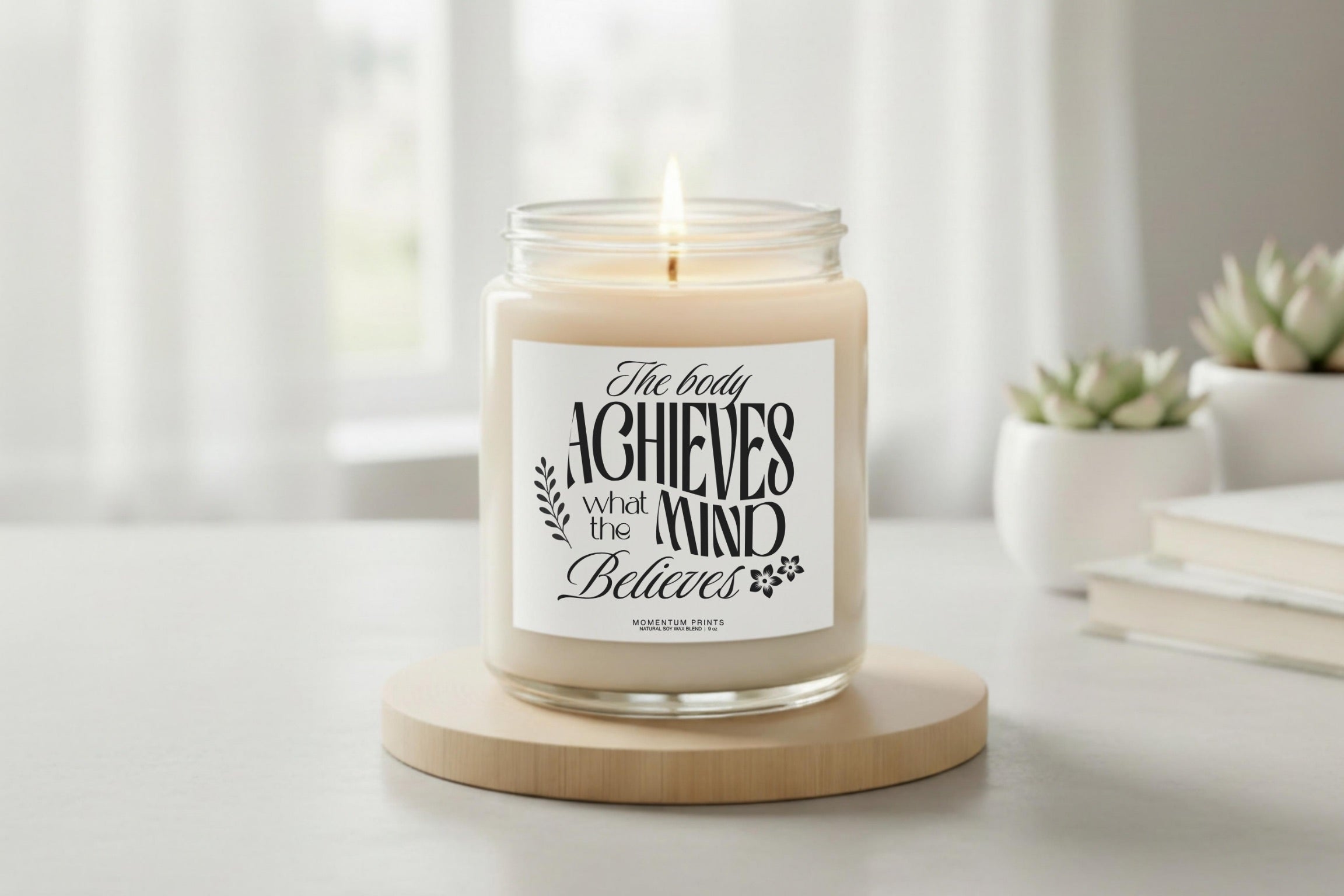 Motivational soy candle with “The body achieves what the mind believes” quote on a neutral pedestal in a bright minimalist setting by Momentum Prints.