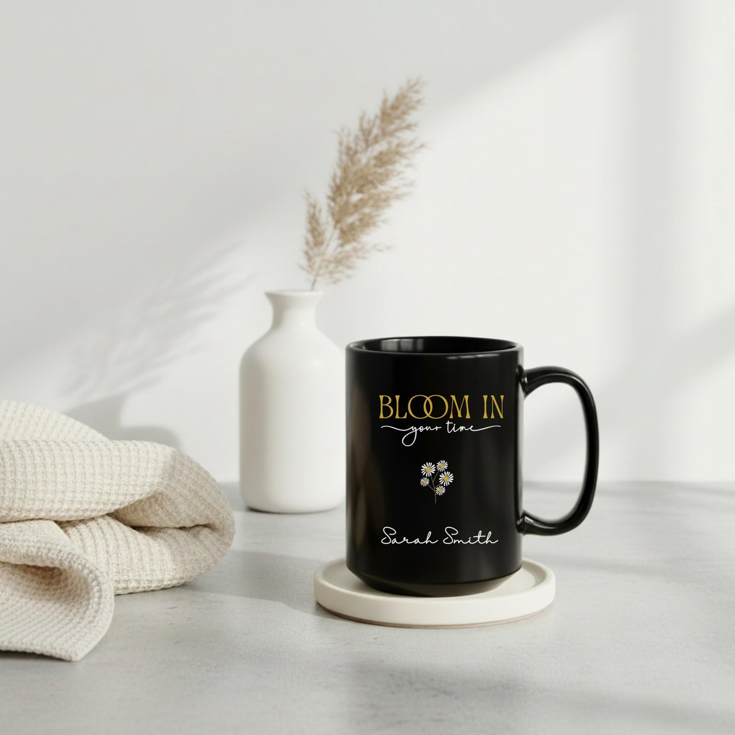 Personalized black ceramic mug with “Bloom in Your Time” design in gold and white lettering, styled on a neutral tray with a white vase and soft knit blanket in a cozy minimalist setting.