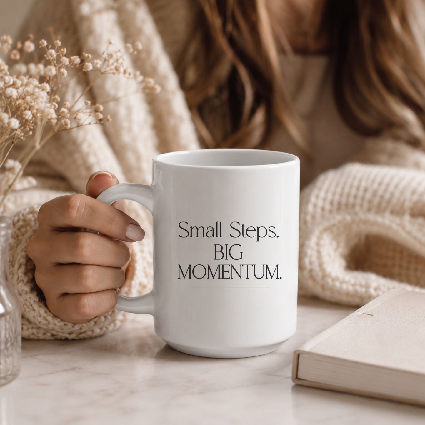 Woman holding a Small Steps. BIG MOMENTUM. white ceramic mug in a cozy neutral-toned setting, creating a warm and inspiring lifestyle moment. Momentum Prints.