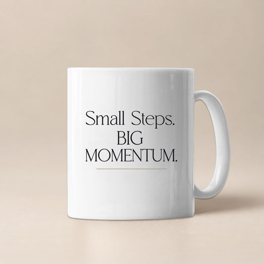 White ceramic mug displaying the Small Steps. BIG MOMENTUM. design against a soft beige background.