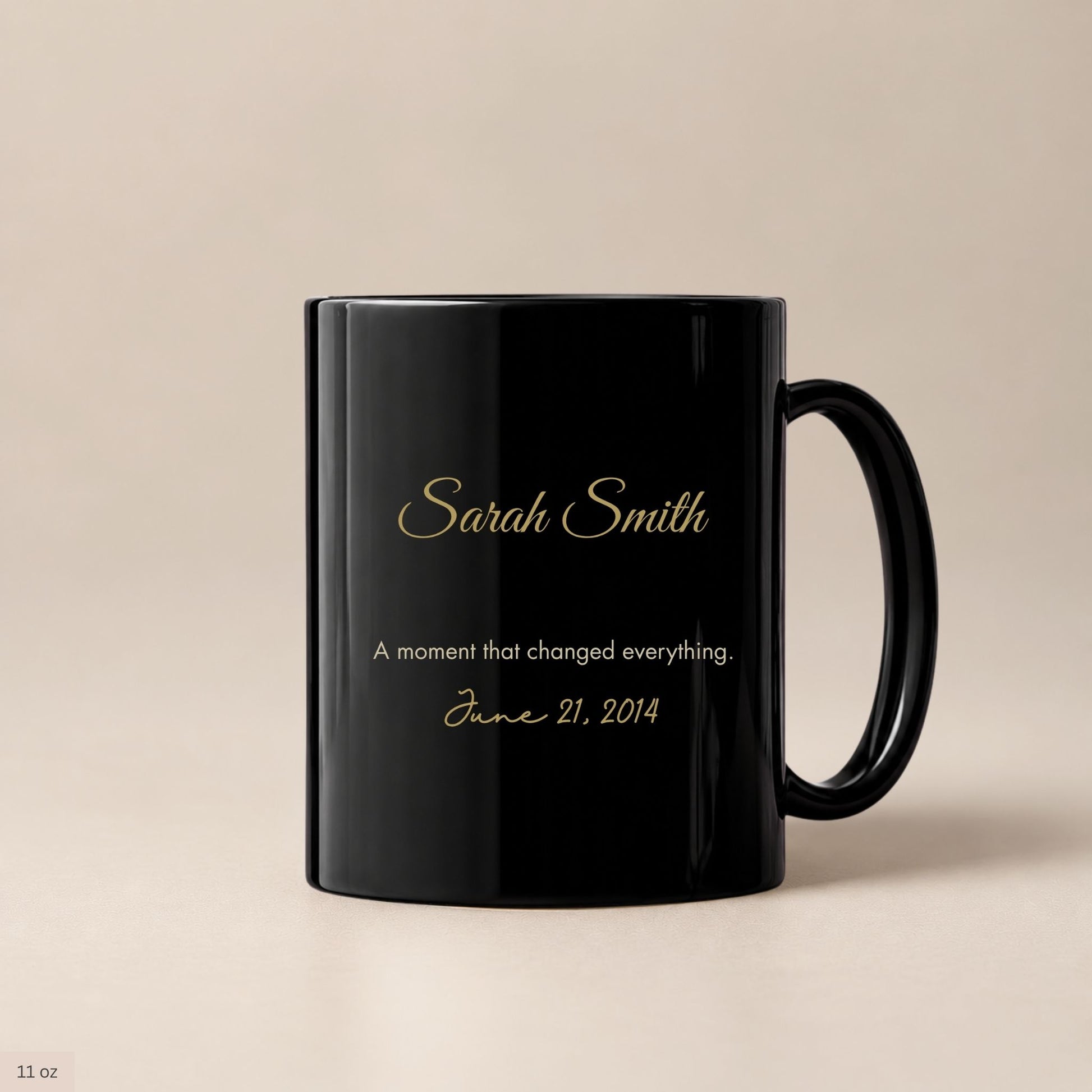 Personalized black ceramic coffee mug with gold cursive name and a cream inscription marking a life changing date, photographed against a warm neutral background by Momentum Prints.