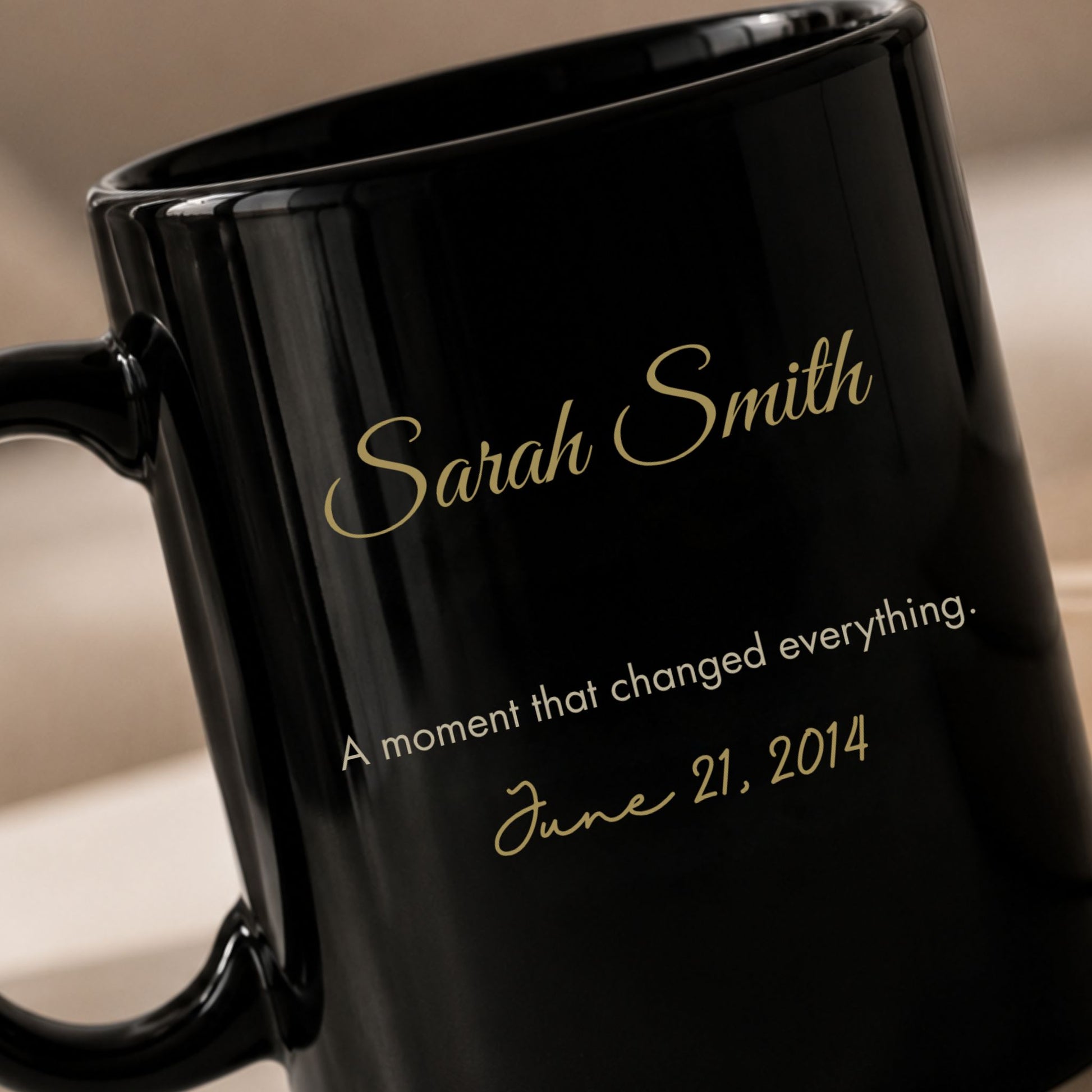 Close up detail of a black ceramic mug showing a personalized gold script name and cream inscription commemorating a meaningful date by Momentum Prints.