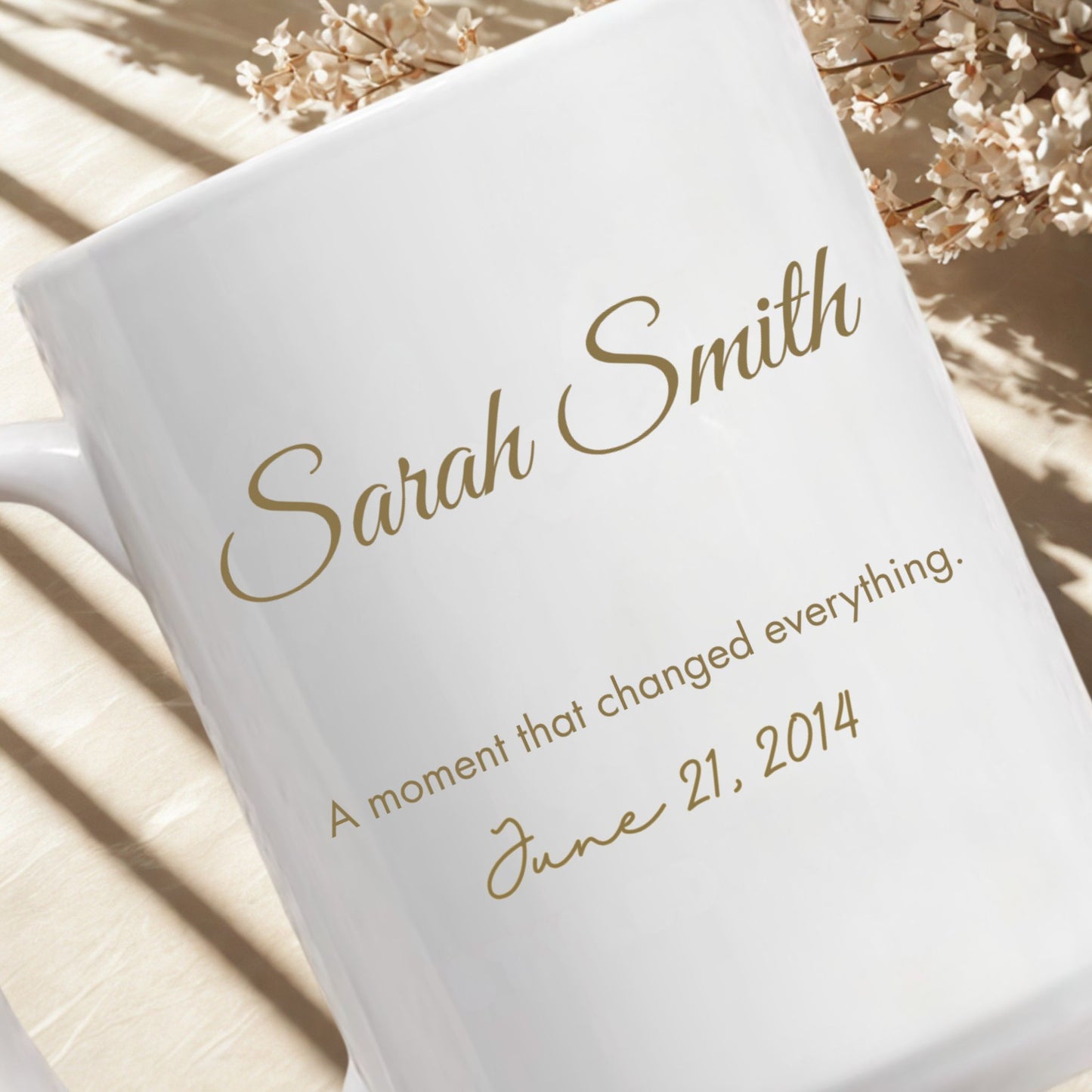Personalized white mug with custom name and special date in gold typography, photographed in soft natural light with neutral floral styling.