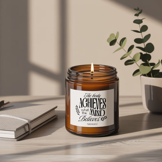 The Body Achieves What the Mind Believes 4 oz amber glass soy candle styled on a minimalist desk with eucalyptus and soft natural lighting.