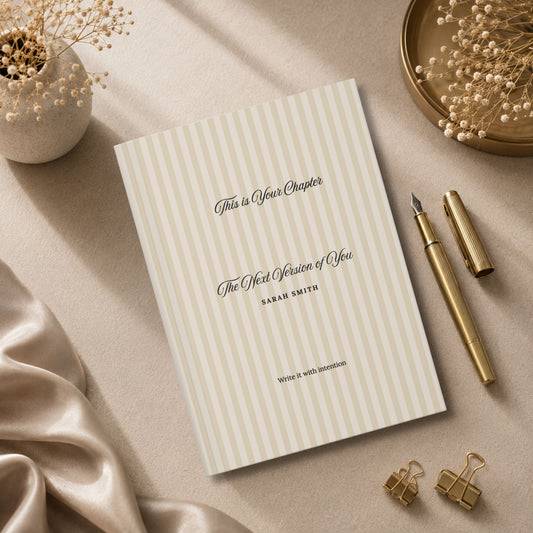 Premium personalized hardcover journal with beige striped cover standing beside champagne gold pen, matte ceramic vase and beige silk fabric in a luxury editorial lifestyle setting by Momentum Prints