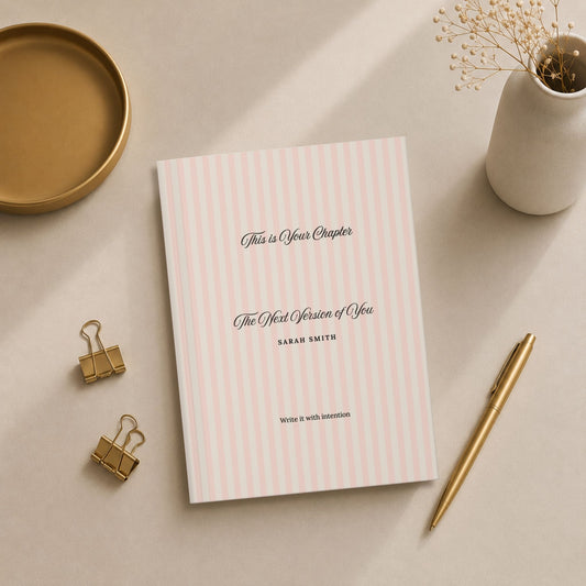 Premium personalized hardcover journal with dusty rose striped cover styled in a flat lay with a gold pen, gold binder clips, a small gold dish, and a ceramic vase with dried flowers by Momentum Prints.