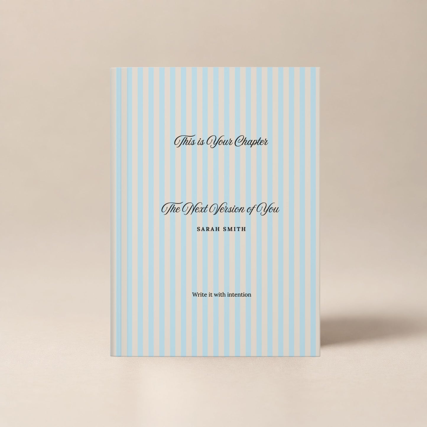 Premium personalized hardcover journal with a sky blue striped cover and black script lettering, shown standing upright on a soft beige background by Momentum Prints.