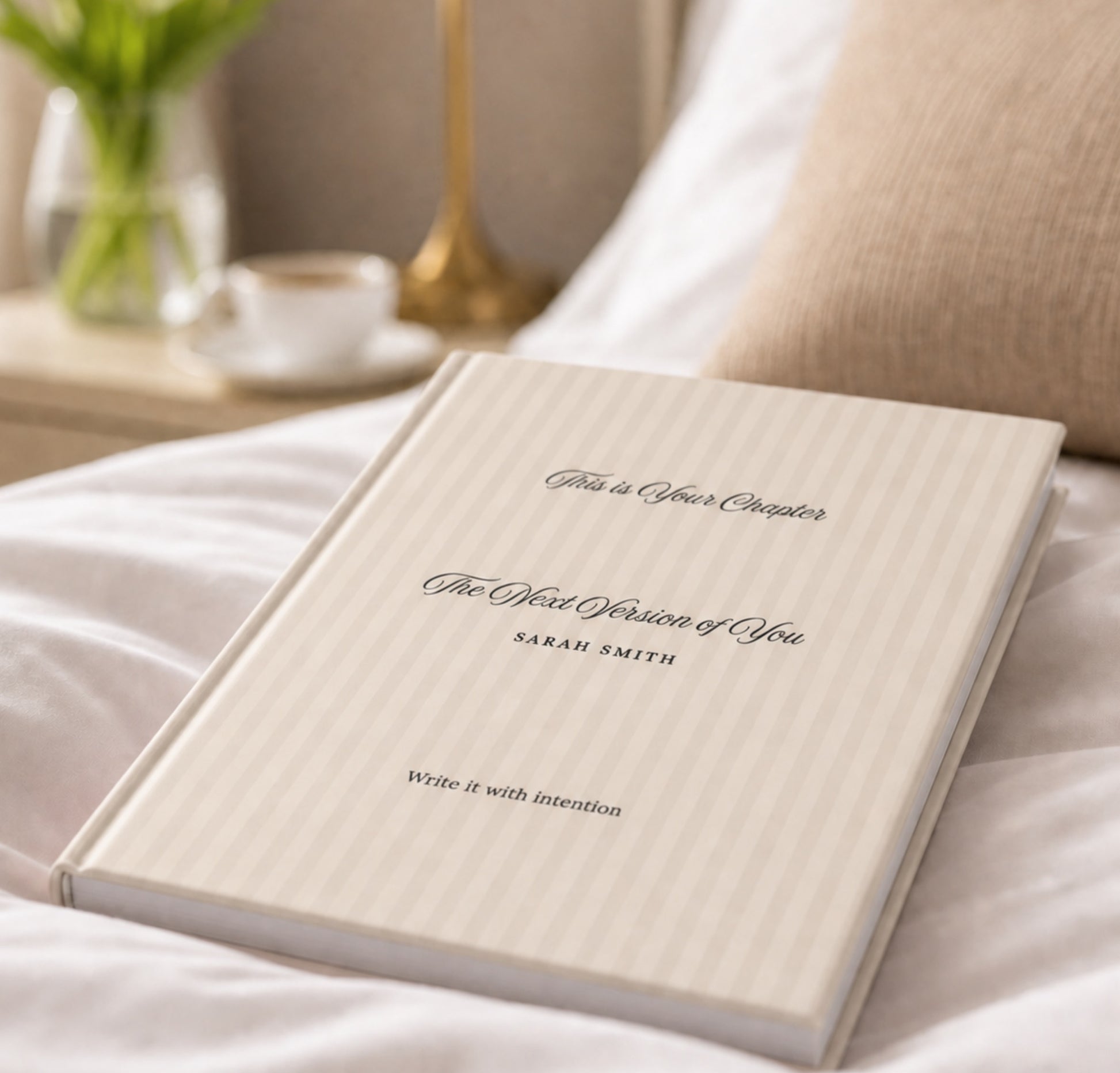 Premium personalized hardcover journal with soft beige striped cover resting on a bed, styled beside a cup of coffee, fresh greenery, and a warm knit pillow in a cozy lifestyle setting by Momentum Prints.