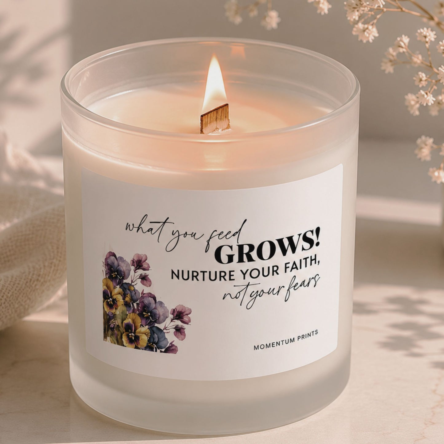 Frosted glass candle with wooden wick flame and “What You Feed Grows” floral design, photographed in a soft beige minimalist setting with delicate dried flowers by Momentum Prints.