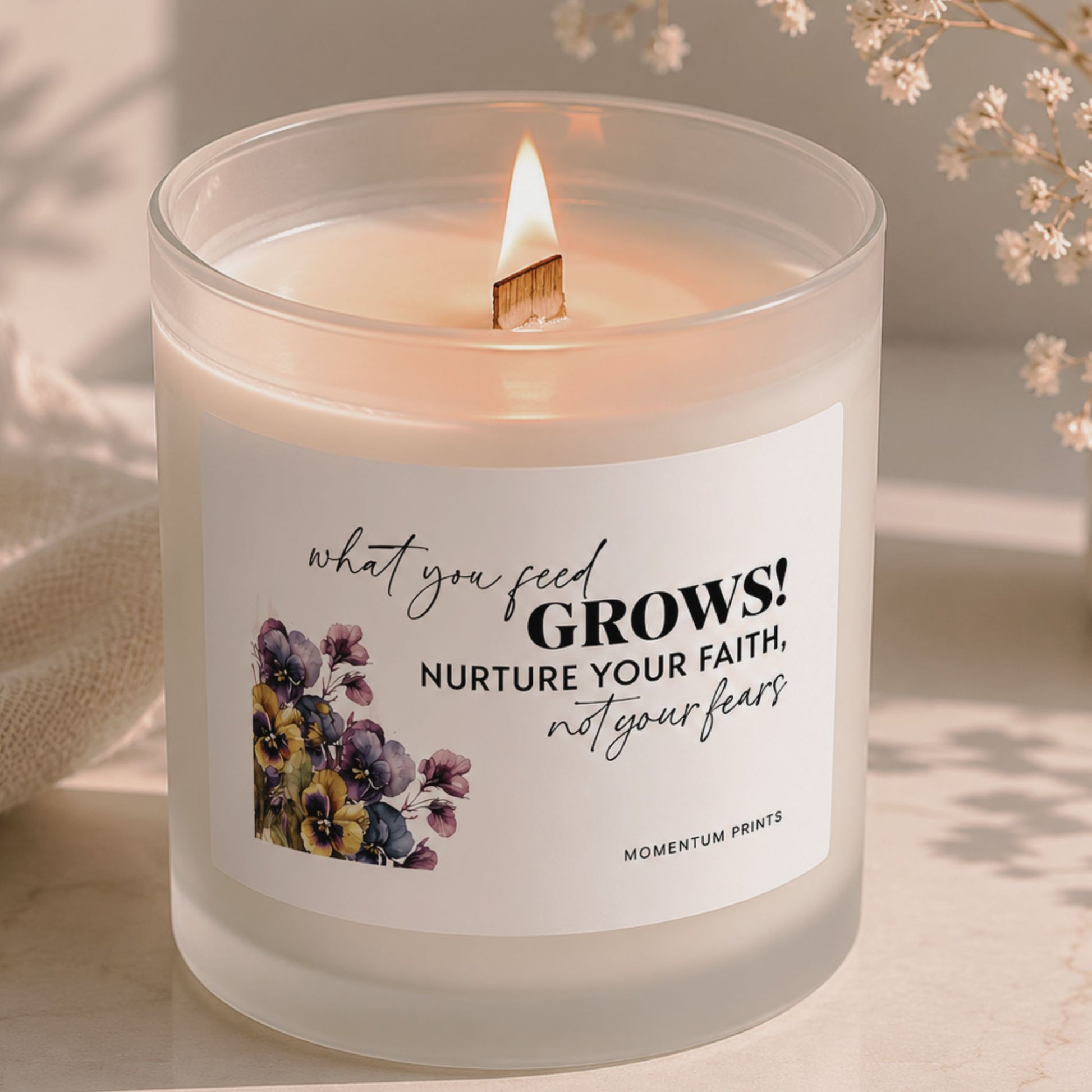 Frosted glass candle with wooden wick flame and “What You Feed Grows” floral design, photographed in a soft beige minimalist setting with delicate dried flowers by Momentum Prints.