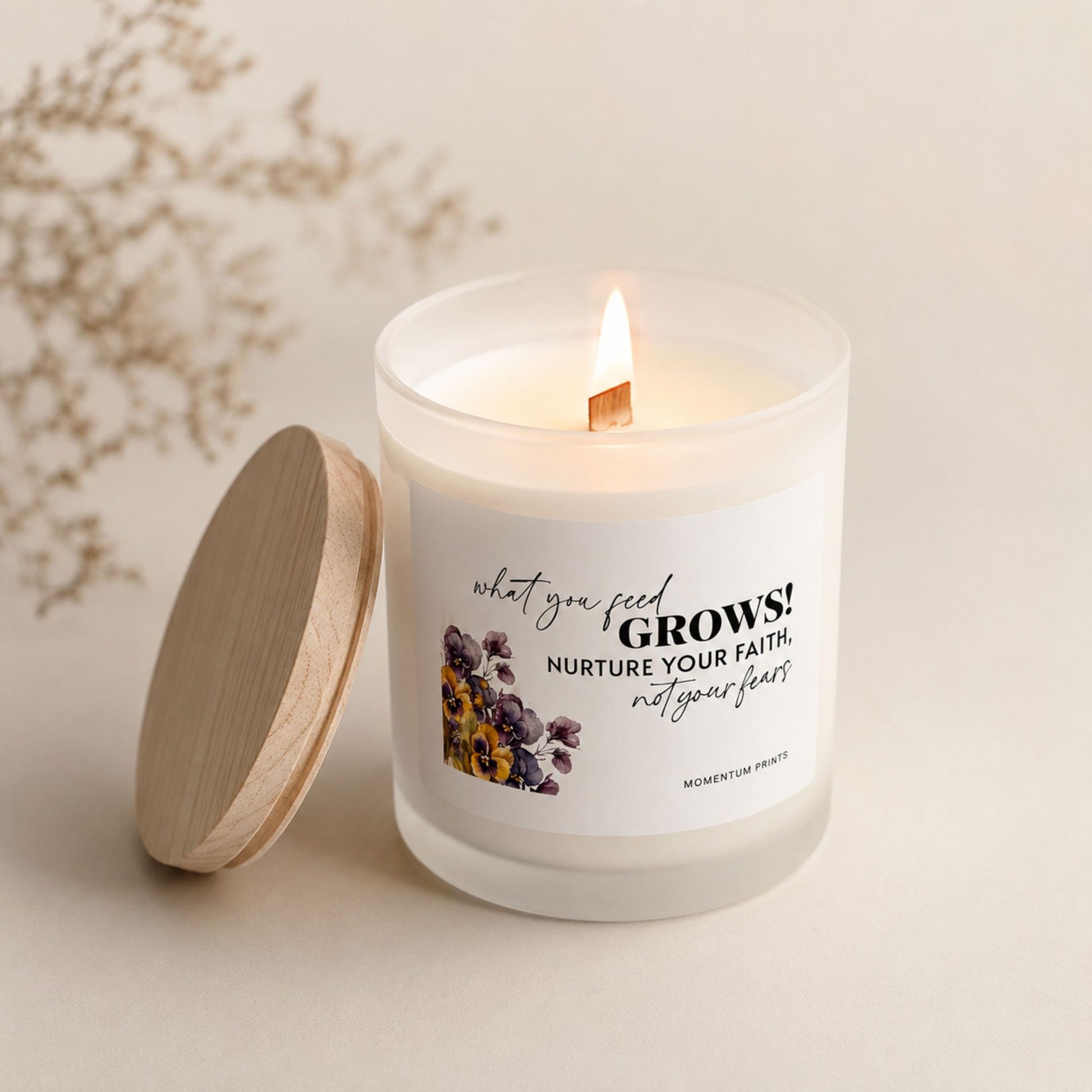 Lit frosted glass candle with wooden wick and “What You Feed Grows” label, styled in a warm cozy neutral setting with soft natural light by Momentum Prints.